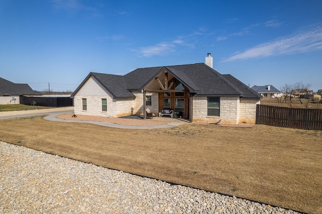 view of front of home with stone siding, roof with shingles, fence, and a chimney