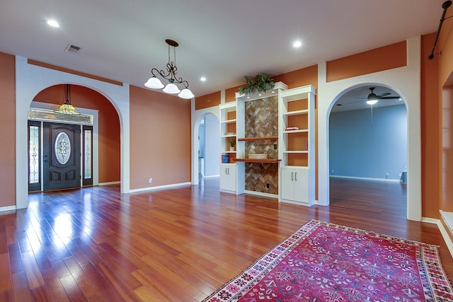 unfurnished living room with hardwood / wood-style flooring, ceiling fan with notable chandelier, and built in features