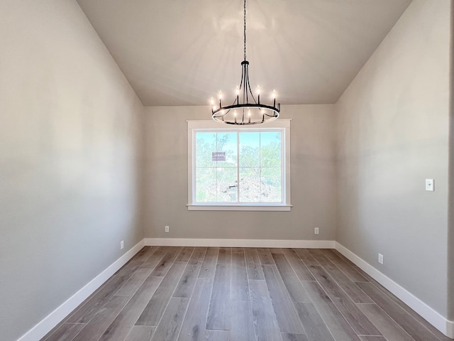 unfurnished dining area with a notable chandelier, vaulted ceiling, wood finished floors, and baseboards