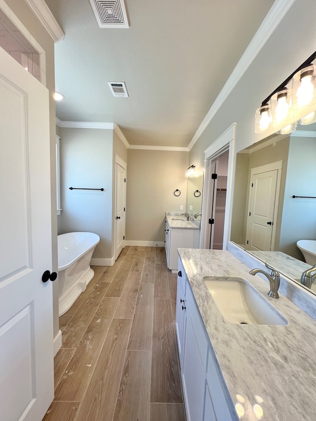 bathroom with ornamental molding, wood finished floors, a sink, a freestanding bath, and two vanities