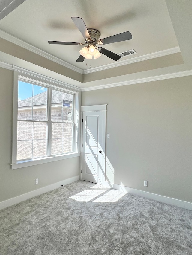 carpeted spare room featuring ornamental molding, a raised ceiling, visible vents, and baseboards