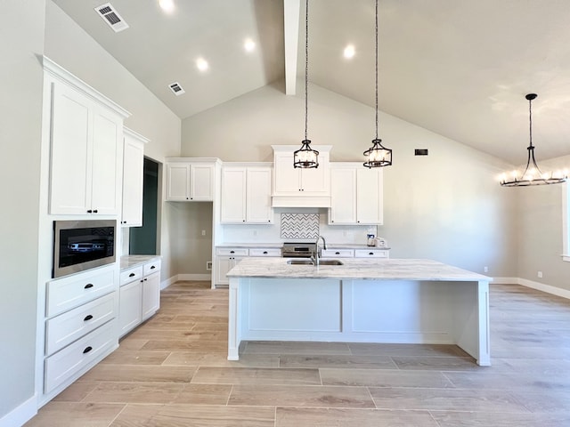 kitchen with visible vents, an island with sink, decorative light fixtures, and white cabinetry