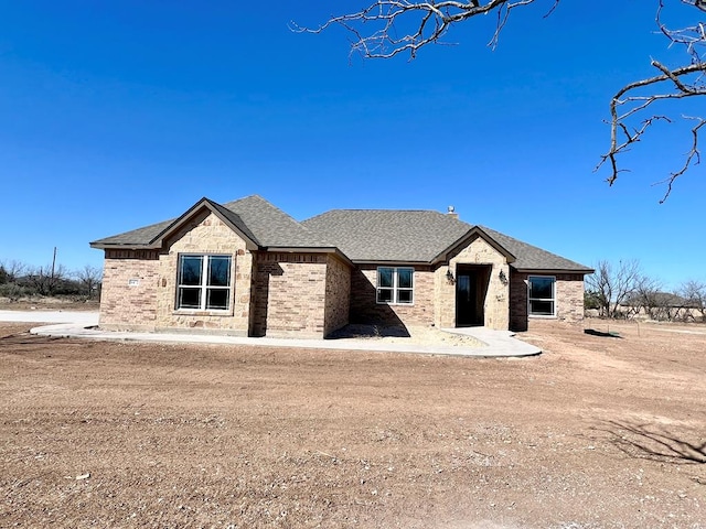 view of front of home featuring brick siding and roof with shingles