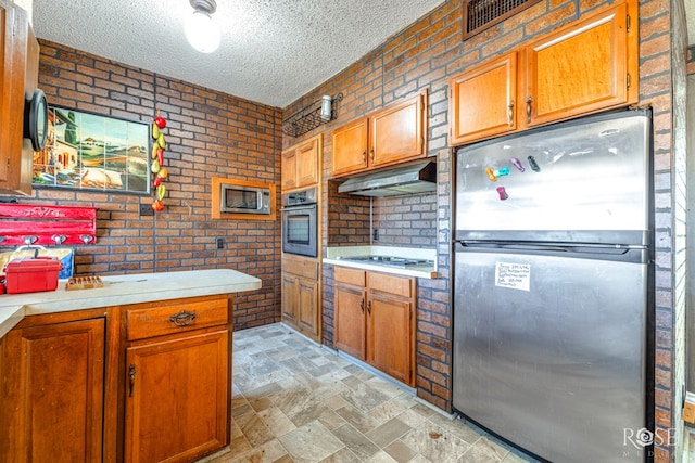 kitchen with brick wall, stainless steel appliances, and a textured ceiling