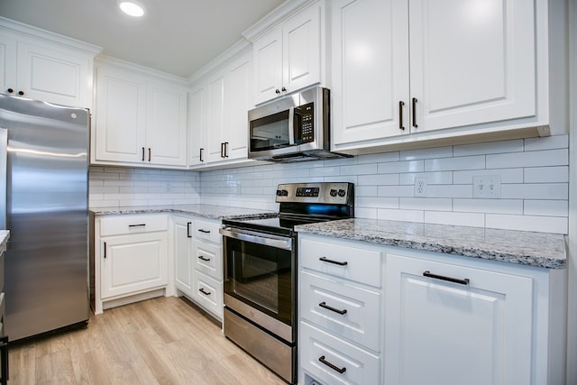 909 E 39th St, San Angelo, TX 76903 - kitchen with stainless steel appliances, white cabinetry, light wood finished floors, decorative backsplash, and light stone counters