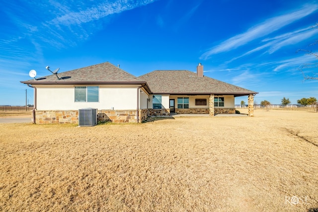 rear view of property featuring stone siding, a chimney, central AC, and stucco siding