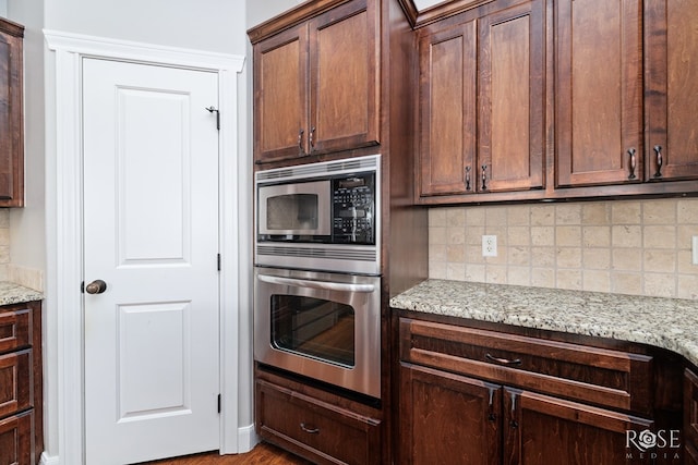 kitchen with light stone counters, stainless steel appliances, dark brown cabinets, and decorative backsplash