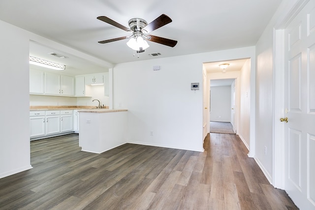 interior space featuring a sink, ceiling fan, a peninsula, white cabinetry, and visible vents