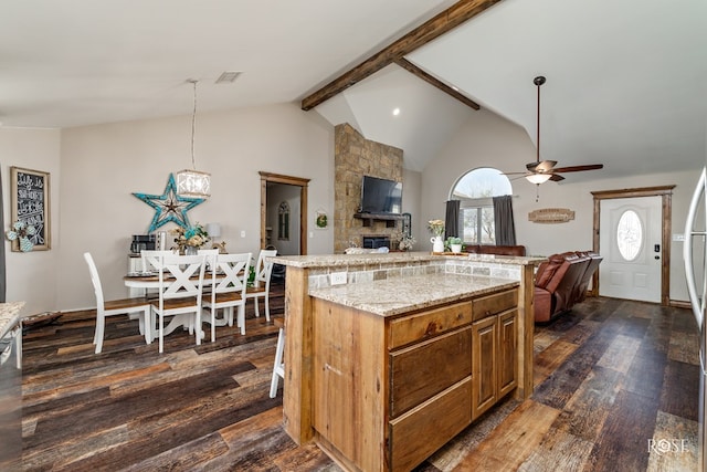 kitchen featuring dark wood-style floors, visible vents, a stone fireplace, beamed ceiling, and open floor plan