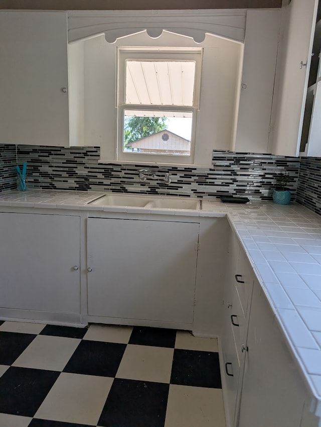 kitchen with tile patterned floors, tile counters, backsplash, and white cabinetry
