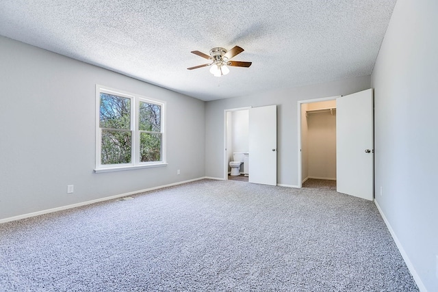 unfurnished bedroom featuring baseboards, ensuite bathroom, a spacious closet, a textured ceiling, and carpet flooring