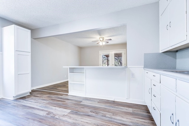 kitchen featuring light wood finished floors, open shelves, light countertops, white cabinetry, and a textured ceiling