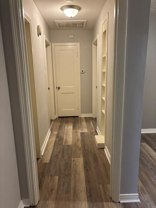 corridor with dark wood-style flooring, visible vents, and baseboards