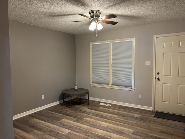 spare room featuring baseboards, visible vents, a ceiling fan, dark wood finished floors, and a textured ceiling