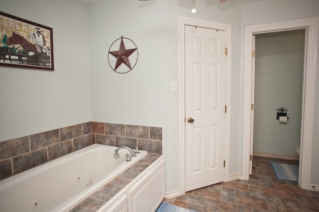 10581 Ballard Rd, San Angelo, TX 76901 - full bathroom with a jetted tub, stone finish flooring, baseboards, and toilet