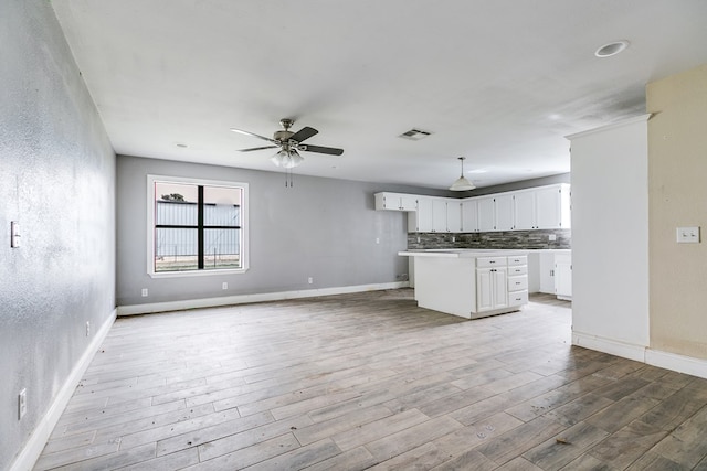 kitchen featuring visible vents, light wood-style flooring, backsplash, a kitchen island, and white cabinetry