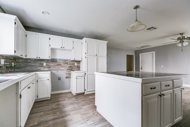 kitchen featuring visible vents, a kitchen island, backsplash, wood finished floors, and white cabinetry