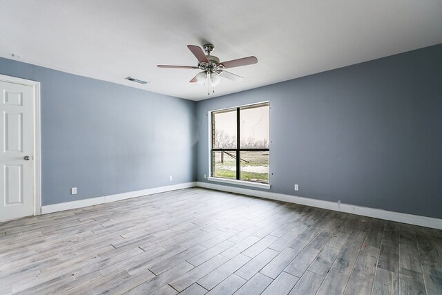 empty room with a ceiling fan, wood finished floors, visible vents, and baseboards