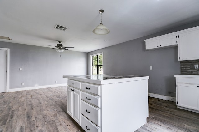 kitchen with white cabinetry, wood finished floors, visible vents, and baseboards