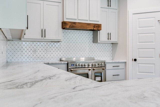 kitchen featuring double oven range, backsplash, and light stone counters