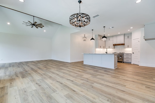 kitchen with gray cabinets, pendant lighting, tasteful backsplash, a kitchen island with sink, and light hardwood / wood-style floors