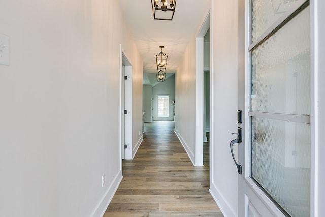 hallway with an inviting chandelier, hardwood / wood-style floors, and vaulted ceiling