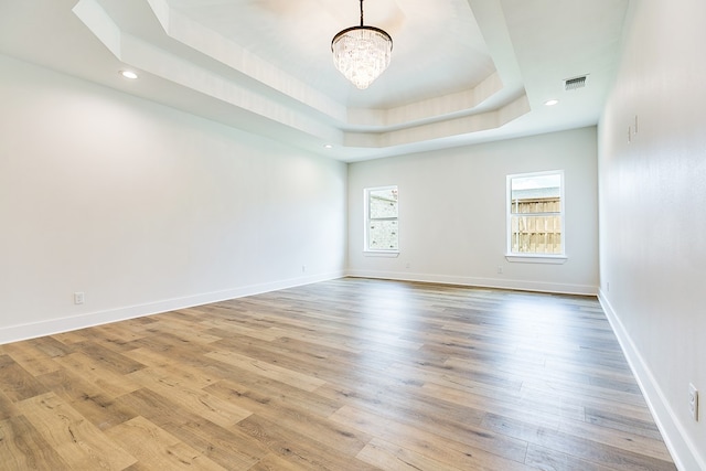 unfurnished room featuring a notable chandelier, a tray ceiling, light hardwood / wood-style flooring, and a wealth of natural light