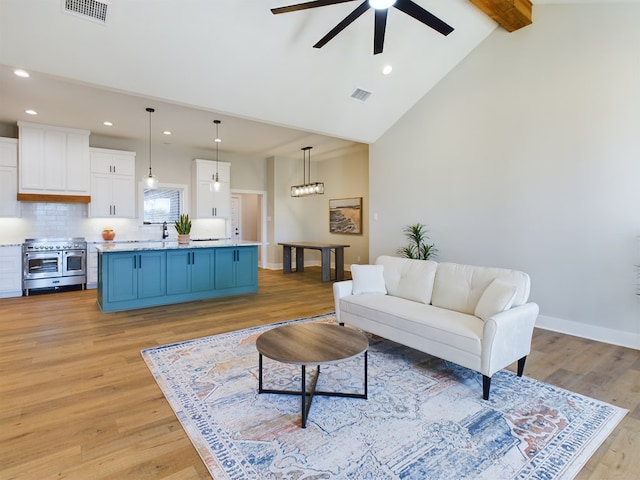 living room featuring sink, ceiling fan, high vaulted ceiling, beamed ceiling, and light wood-type flooring