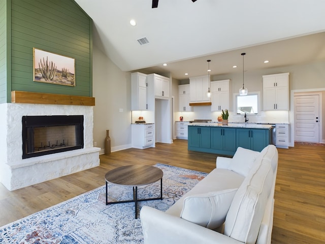 living room with sink, vaulted ceiling, light hardwood / wood-style flooring, ceiling fan, and a fireplace