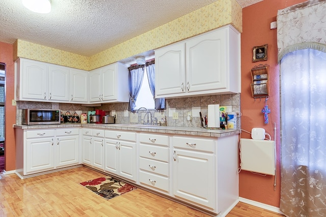 kitchen with sink, light hardwood / wood-style flooring, a textured ceiling, white cabinets, and decorative backsplash