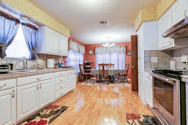 kitchen featuring hanging light fixtures, stainless steel electric stove, sink, and white cabinets