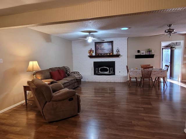 living room featuring dark wood-type flooring, ceiling fan, a brick fireplace, and a textured ceiling