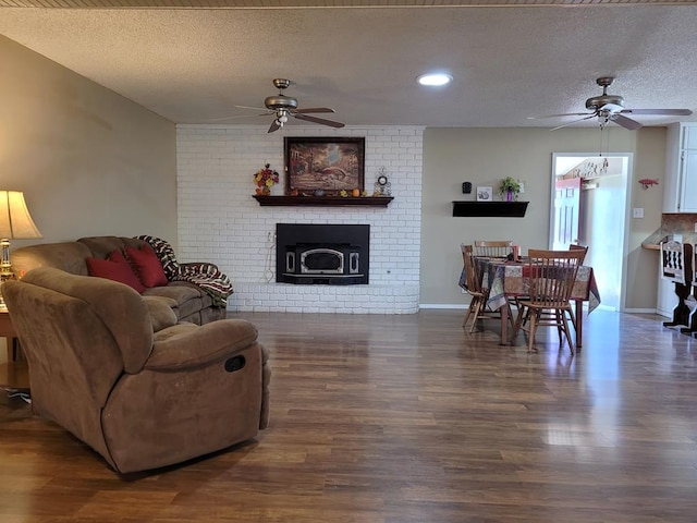 living room with a brick fireplace, a textured ceiling, ceiling fan, and wood finished floors
