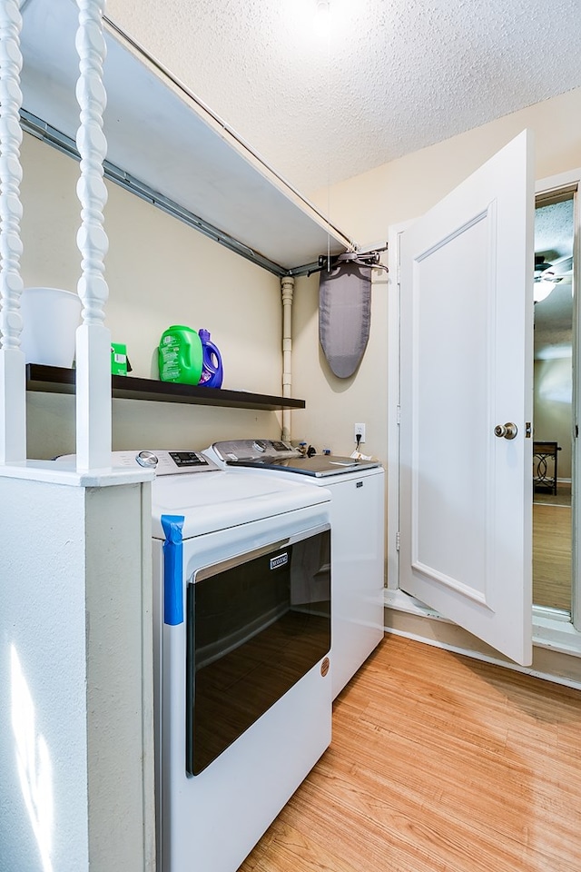 laundry area featuring separate washer and dryer, cabinets, a textured ceiling, and light wood-type flooring