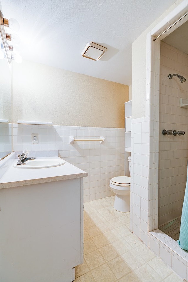 bathroom featuring tile walls, vanity, tiled shower, toilet, and a textured ceiling