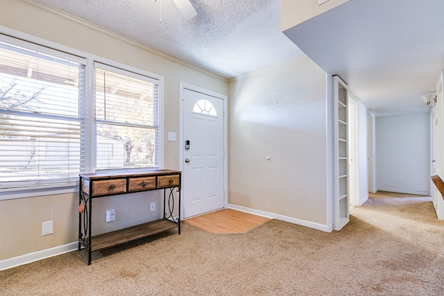 foyer featuring ceiling fan, ornamental molding, light carpet, and a textured ceiling