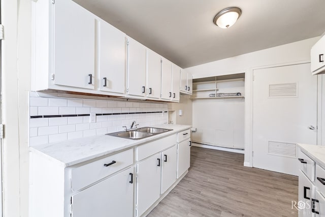 kitchen with sink, tasteful backsplash, light stone counters, white cabinets, and light wood-type flooring