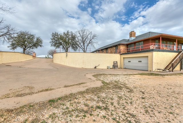 view of side of home with concrete driveway, stucco siding, an attached garage, and a chimney