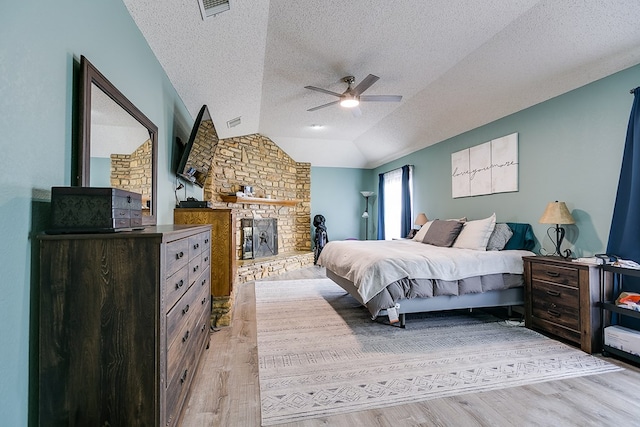 bedroom with light wood finished floors, visible vents, a textured ceiling, and lofted ceiling