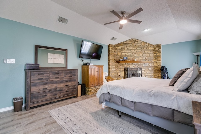 bedroom featuring visible vents, lofted ceiling, a fireplace, wood finished floors, and a textured ceiling