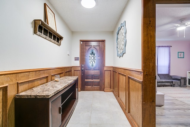 foyer entrance featuring a wainscoted wall, a textured ceiling, and ceiling fan