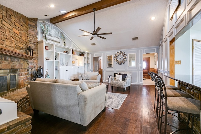 living room featuring visible vents, dark wood-style floors, a stone fireplace, a decorative wall, and vaulted ceiling with beams