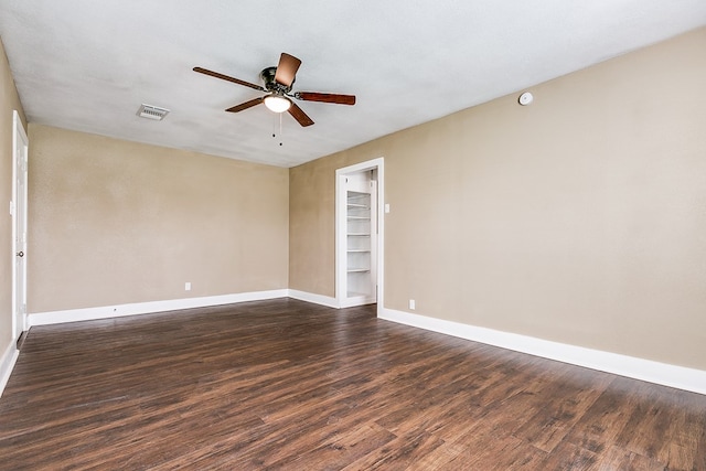 spare room with a ceiling fan, dark wood-style flooring, visible vents, and baseboards