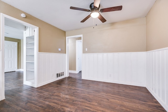 unfurnished room featuring a ceiling fan, a wainscoted wall, visible vents, and dark wood finished floors