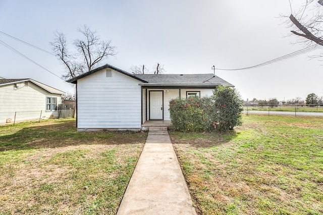 view of front facade featuring a front yard, roof with shingles, and fence