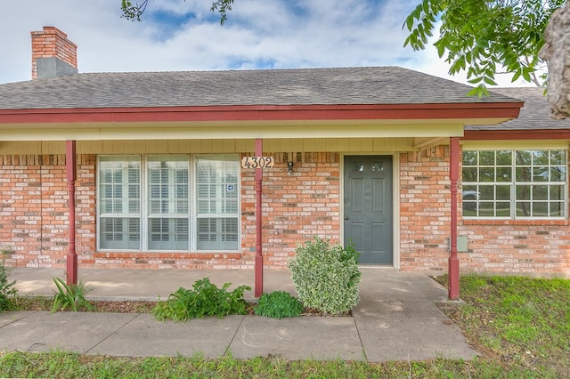 4302 Homestead Cir, Wall, TX 76903 - view of exterior entry with a shingled roof, brick siding, and a chimney