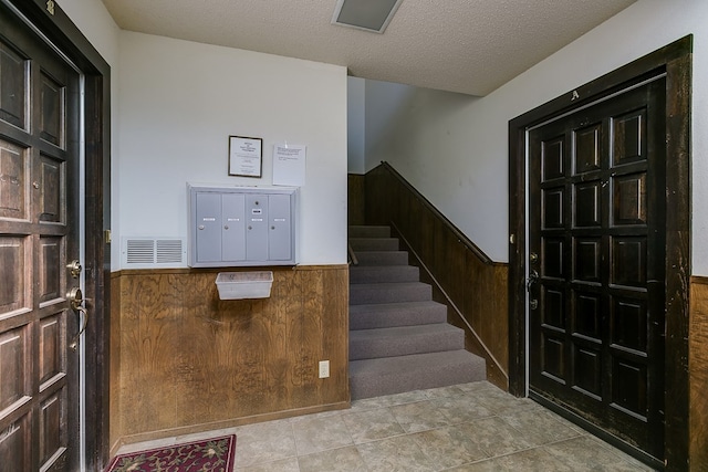 foyer featuring a mail area, a textured ceiling, and wood walls