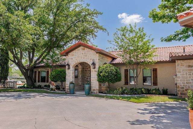 mediterranean / spanish house featuring stone siding, a tile roof, and stucco siding