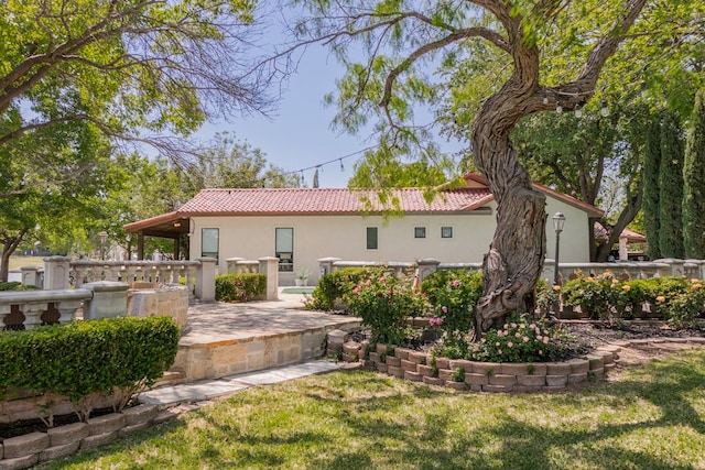rear view of property with stucco siding, a yard, and a tiled roof