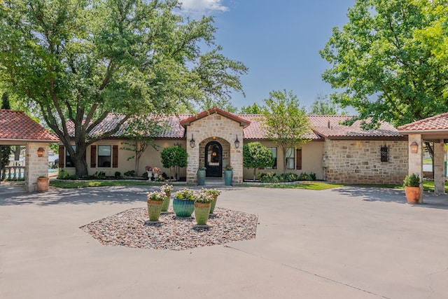 mediterranean / spanish home with stone siding, a tile roof, curved driveway, and stucco siding